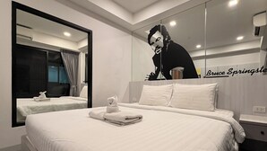 Ein Hotelzimmer mit einem großen Bett, einem kleineren Bett, einem Spiegel, einem Wandbild und einem Nachttisch.