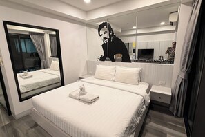 A hotel room with a large mirror, a bed with white linens, a nightstand, and a TV. - Frankie's Inn (Pattaya)