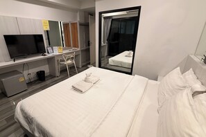 Habitación de hotel con cama, escritorio con televisor, silla y puerta corredera a un balcón.