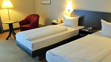 Une chambre d’hôtel avec deux lits simples, un fauteuil rouge, une petite table et des lampes de chevet.