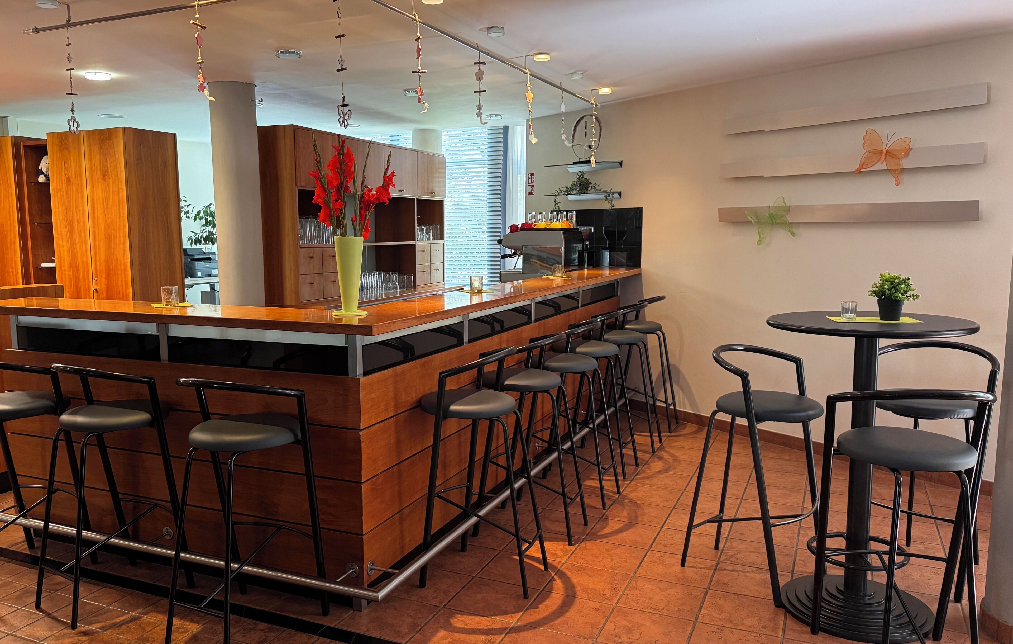 A modern bar area with wooden bar counter, black stools, and a round table with chairs.