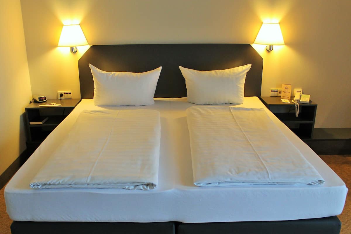 A double bed with two pillows, a bedside table with a lamp, and a phone.
