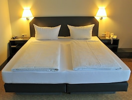 Uma cama de casal com duas almofadas, uma mesa de cabeceira com abajur e um telefone.