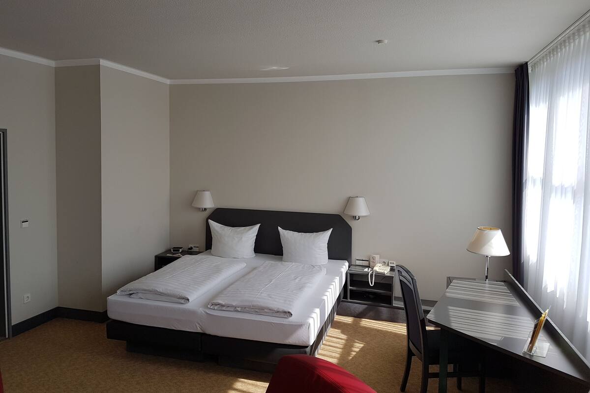 A hotel room with a bed, bedside tables, a desk, and a chair.