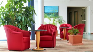 Un vestíbulo con sillas rojas, una mesa y una planta grande.