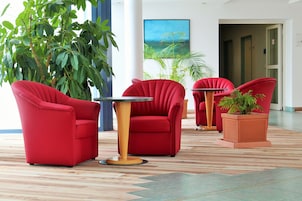 Um hall com cadeiras vermelhas, uma mesa e uma grande planta.