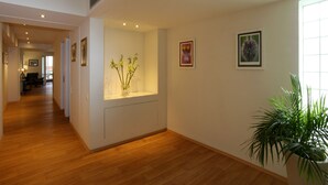 Un couloir avec un plancher en bois, une plante en pot et des œuvres d’art encadrées accrochées aux murs.