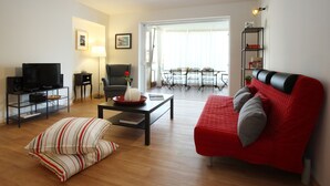 Un salon avec un canapé rouge, un téléviseur, une table basse et un coin repas comprenant une table et des chaises.