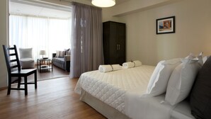 Une chambre d’hôtel avec un grand lit, une chaise, une petite table, une armoire et une fenêtre avec des rideaux.