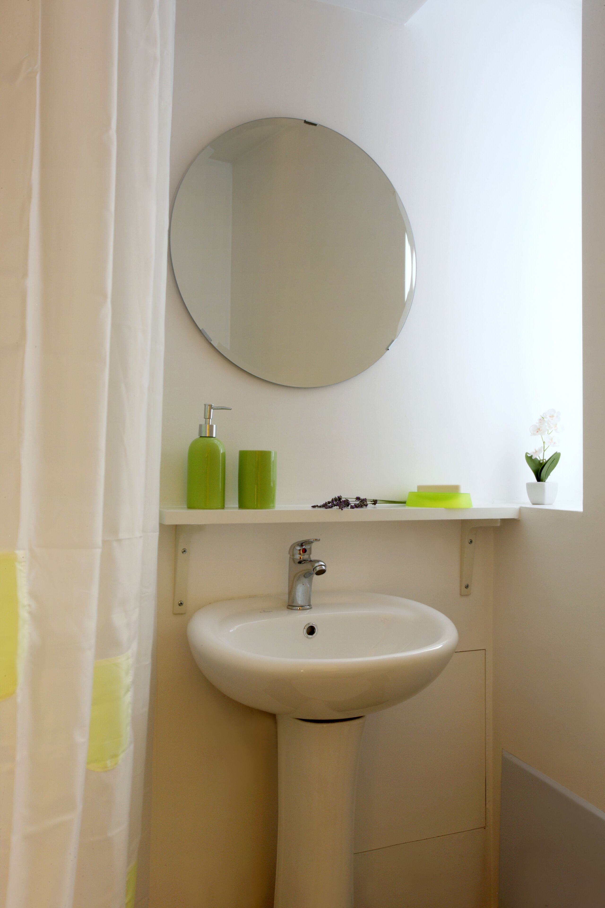 Une salle de bain avec un lavabo blanc, un miroir et une étagère contenant des articles de toilette.