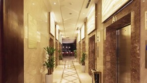 A hotel corridor with marble flooring, potted plants, and an elevator. - Regalia Gold (Nha Trang)