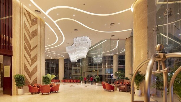 A spacious lobby with modern seating, a large chandelier, and a glass elevator. - Regalia Gold (Nha Trang)