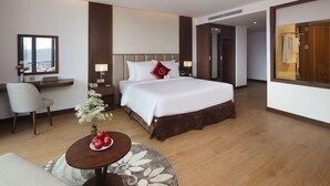 A hotel room with a large bed, bedside tables, a desk, a chair, and a view of the city. - Regalia Gold (Nha Trang)