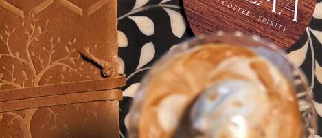 A wooden box with a tree design, a round wooden coaster with "QWAM ART COFFEE SPIRITS" text, and a glass of coffee with a spoon.