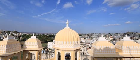 A traditional yellow-domed structure with a central dome and smaller domes on either side, surrounded by a courtyard with seating and potted plants.