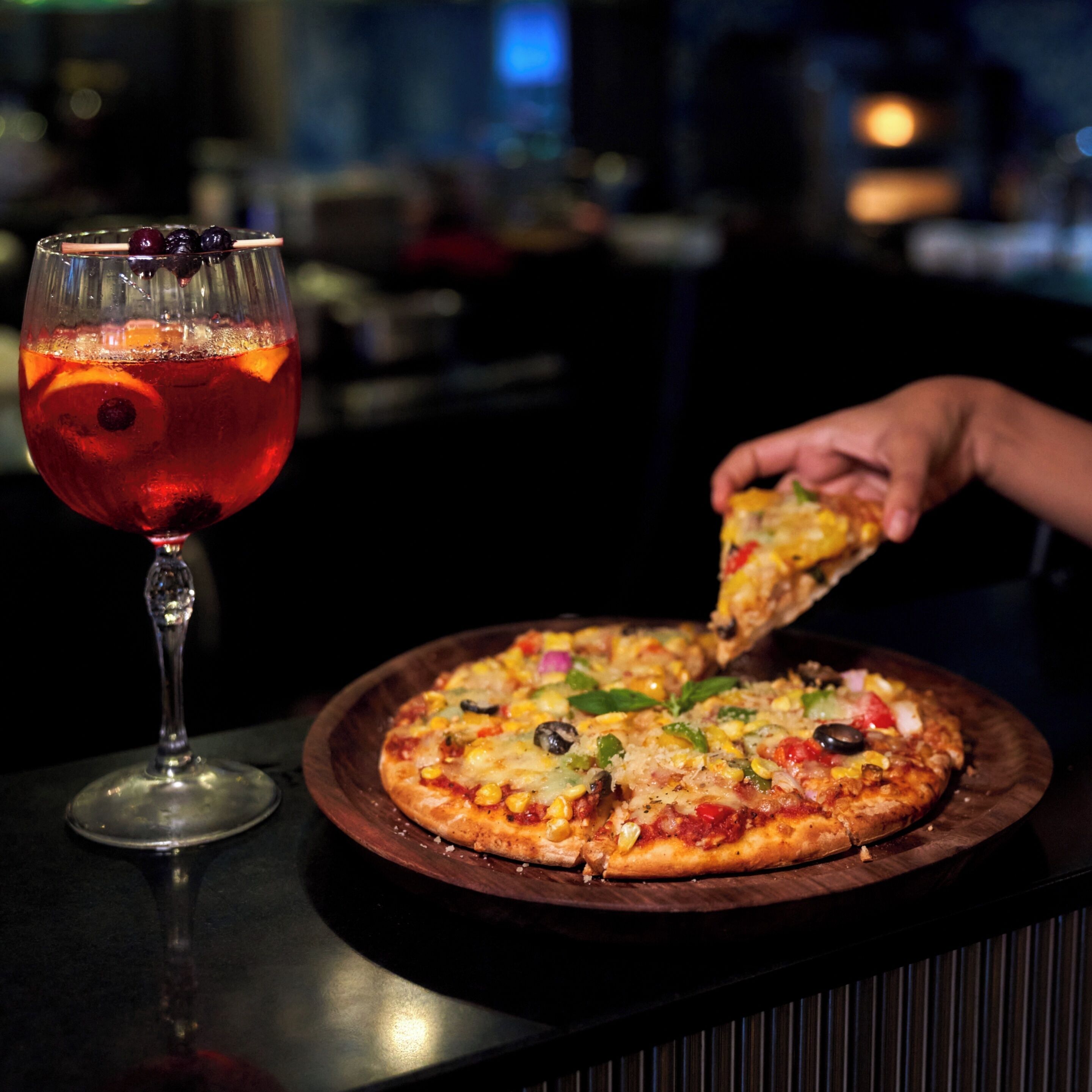 Pizza sobre tábua de madeira com um copo de bebida vermelha ao lado.