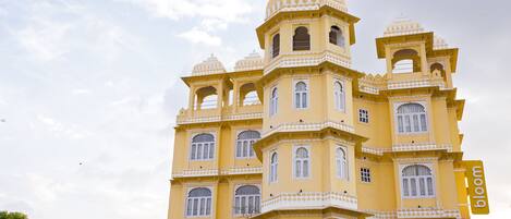 A multi-story building with a yellow facade and white accents, featuring multiple balconies and arched windows.