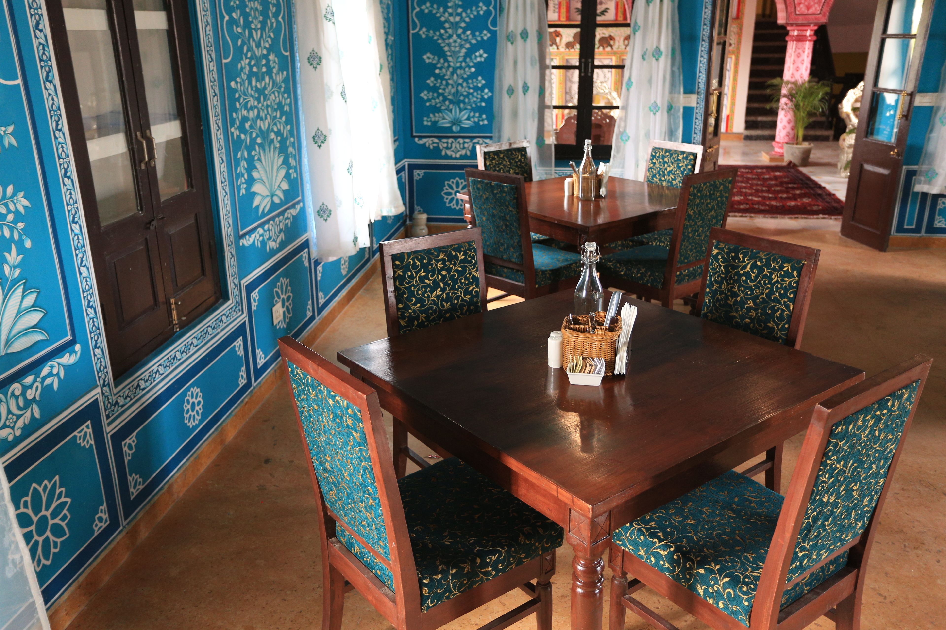 Comedor con mesa y sillas de madera, rodeado de paredes con un estampado azul y una alfombra roja.
