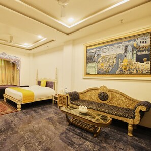 A hotel room with a bed, a sofa, a coffee table, and a large painting on the wall. - Bloom Boutique | Lake Pichola (Udaipur)