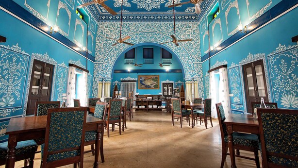 A dining area with blue patterned walls, wooden furniture, and ceiling fans.