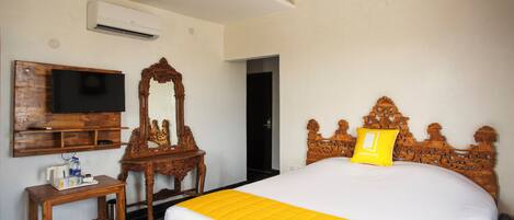 A hotel room with a bed, a television, a mirror, a wooden nightstand, and a door.