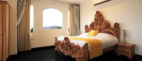 Ein Schlafzimmer mit einem großen Bett, einem Nachttisch, einer Klimaanlage und einem Fenster mit Vorhängen.