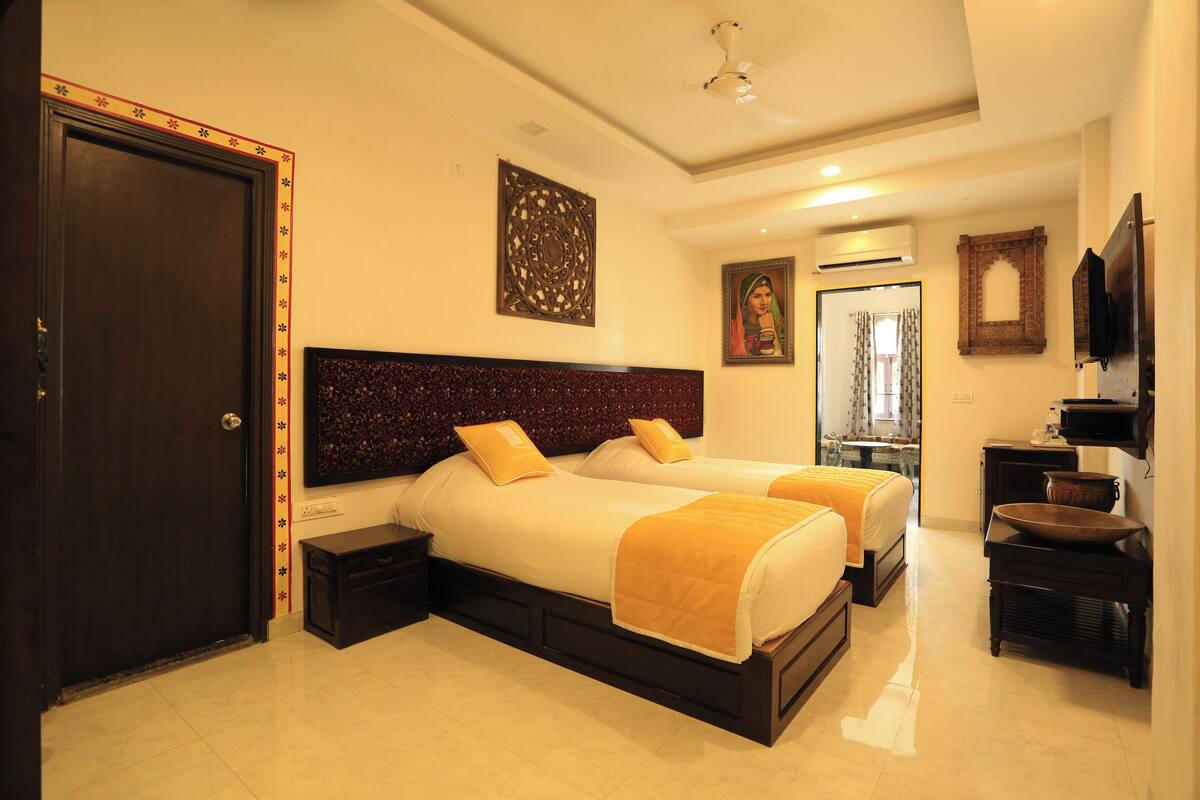 A hotel room with two beds, a dark headboard, a small bedside table, a mirror, and a television.