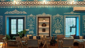 A room with traditional blue and white decor, a ceiling fan, and a seating area with chairs and a sofa.