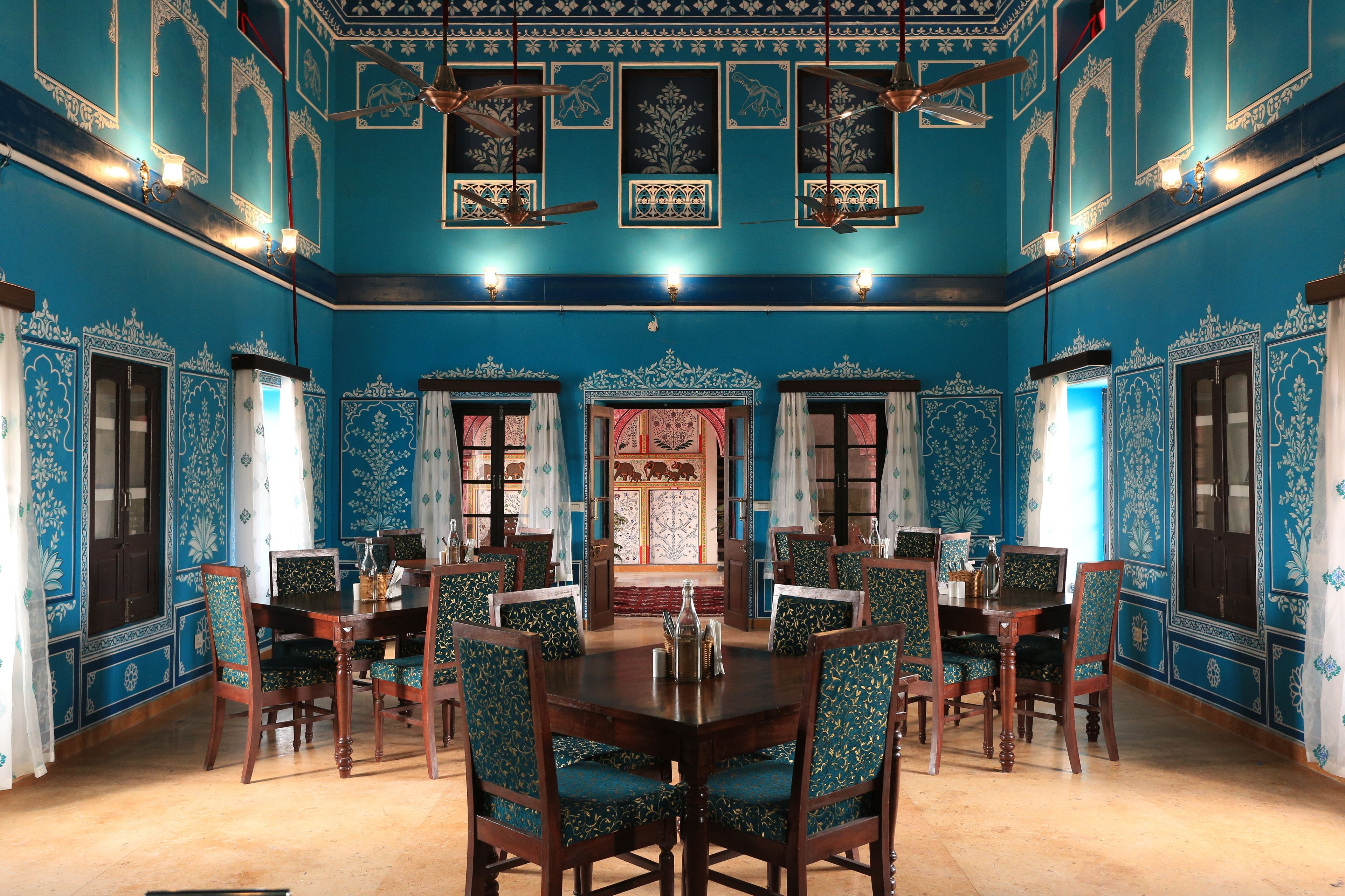 A dining area with a large wooden table and matching chairs, surrounded by blue walls with intricate designs.