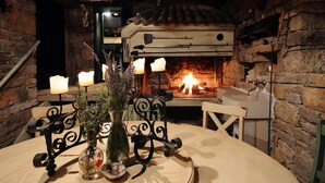 Un interior rústico con pared de piedra, una mesa de madera con un florero y velas, y una chimenea.
