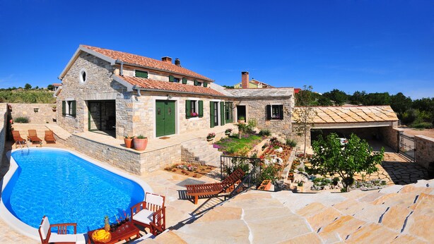 Una villa de piedra con piscina, mobiliario de exterior y jardín.