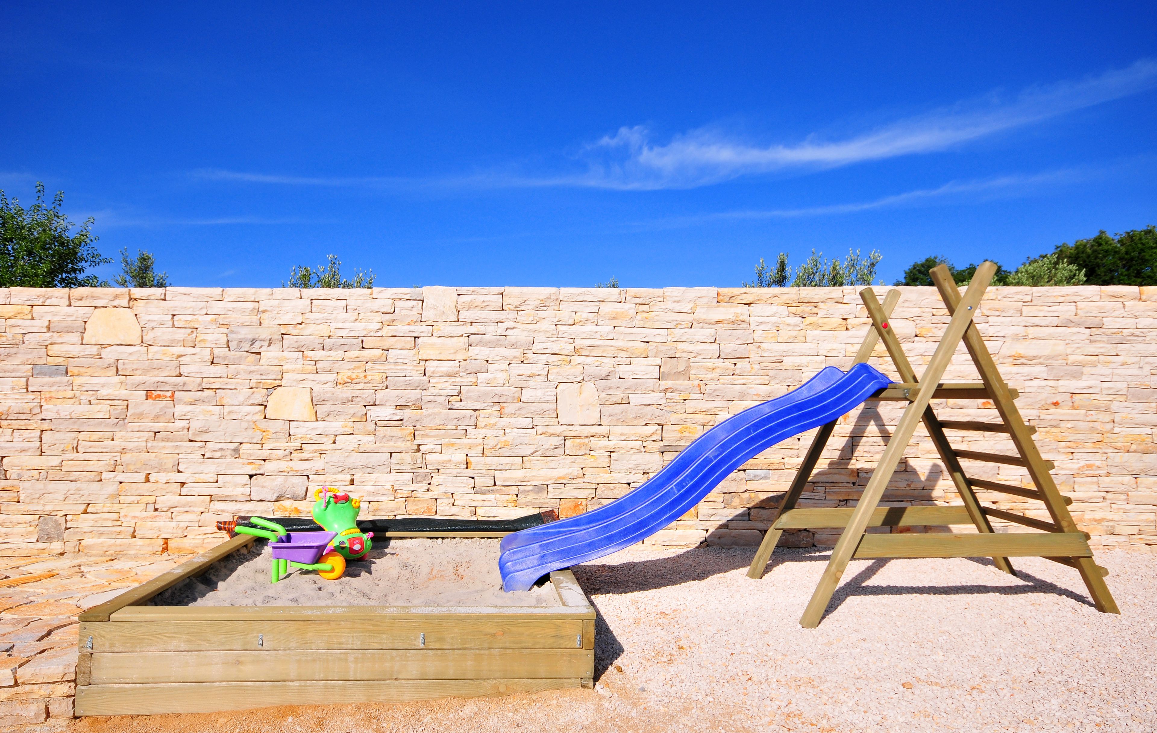 A wooden play area with a slide and a sandpit.