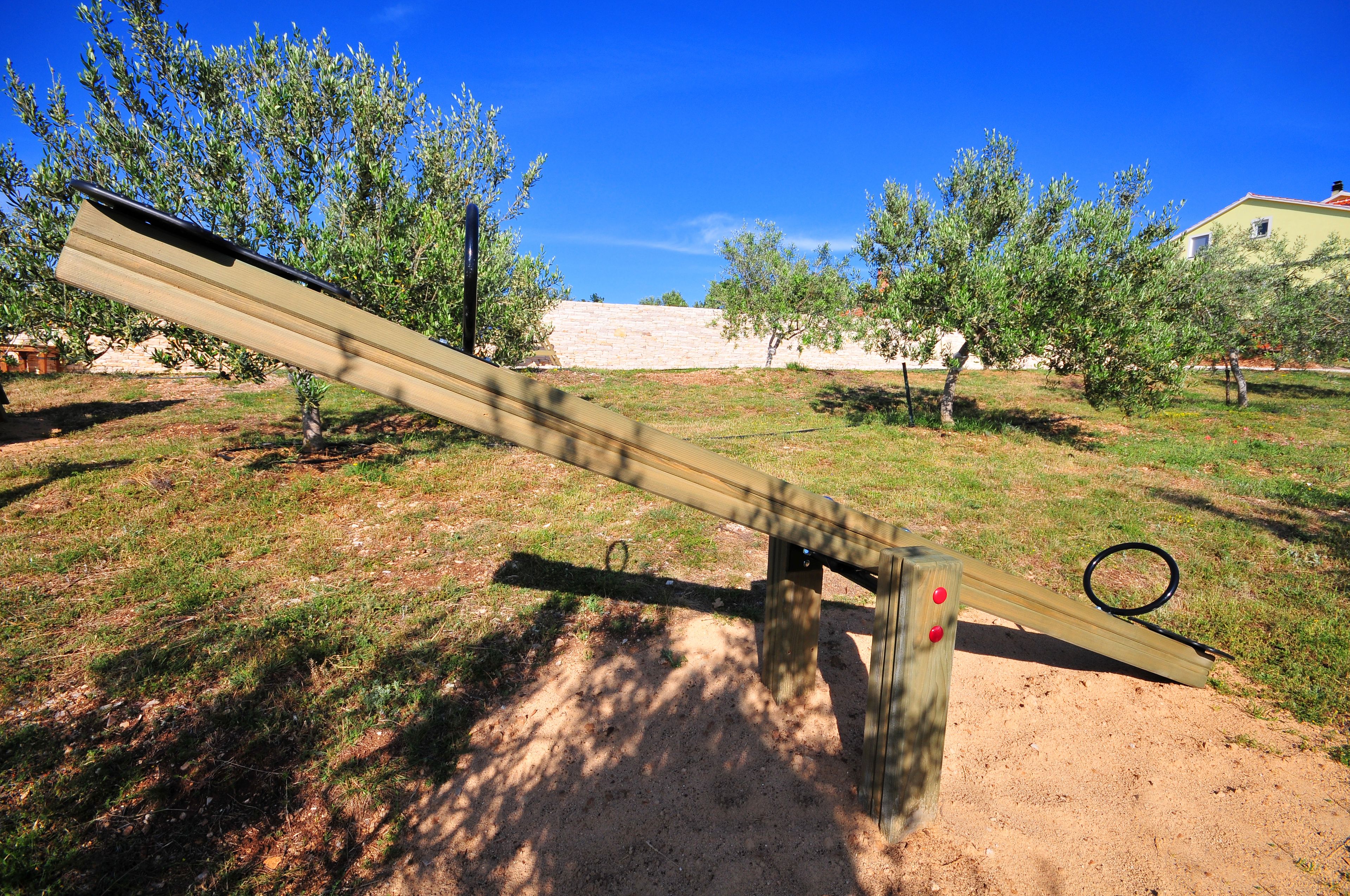 A seesaw in a park with trees and a building in the background.