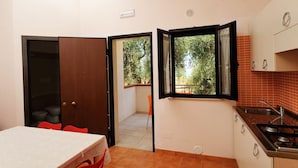 Cocina compacta con comedor, ventana con vistas a árboles y puerta que da a un balcón.