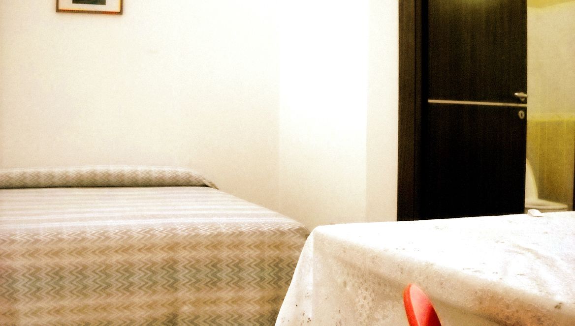 A hotel room with a bed, a small table, and a door.