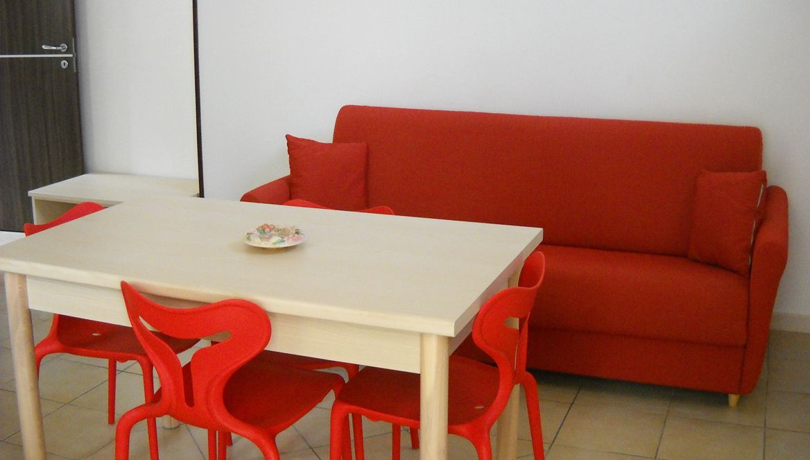 A room with a red sofa, a white table, and red chairs.