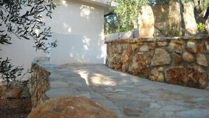 Un sendero de piedra que lleva a un edificio blanco, rodeado de olivos y un muro de piedra.