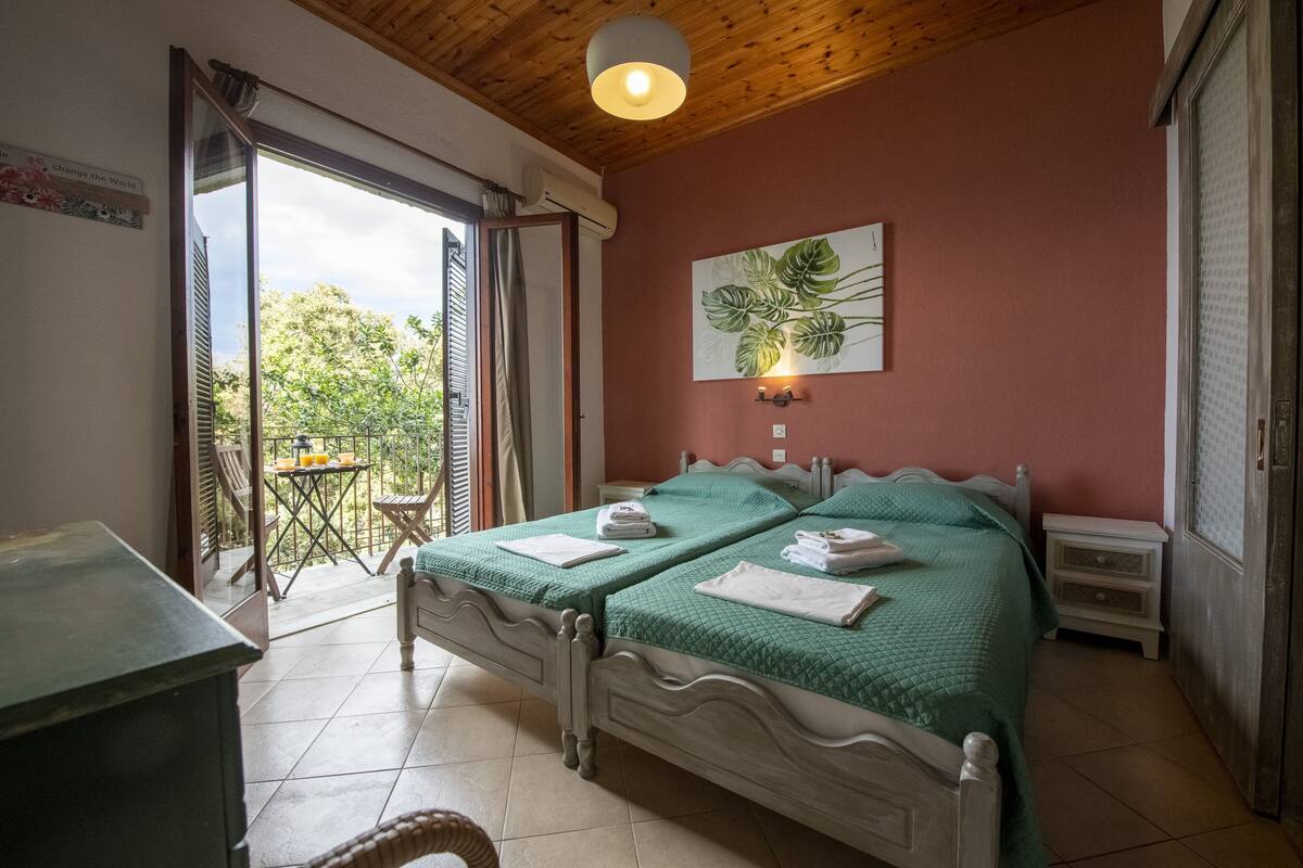 Una camera da letto con due letti, un tavolino, una sedia e vista sull'esterno.