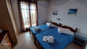 A hotel room with two beds, a window with curtains, a wall-mounted air conditioner, and a small bedside table with a lamp. - Katerina Fotopoulos Homes & Apartments (Zagora-Mouresi)