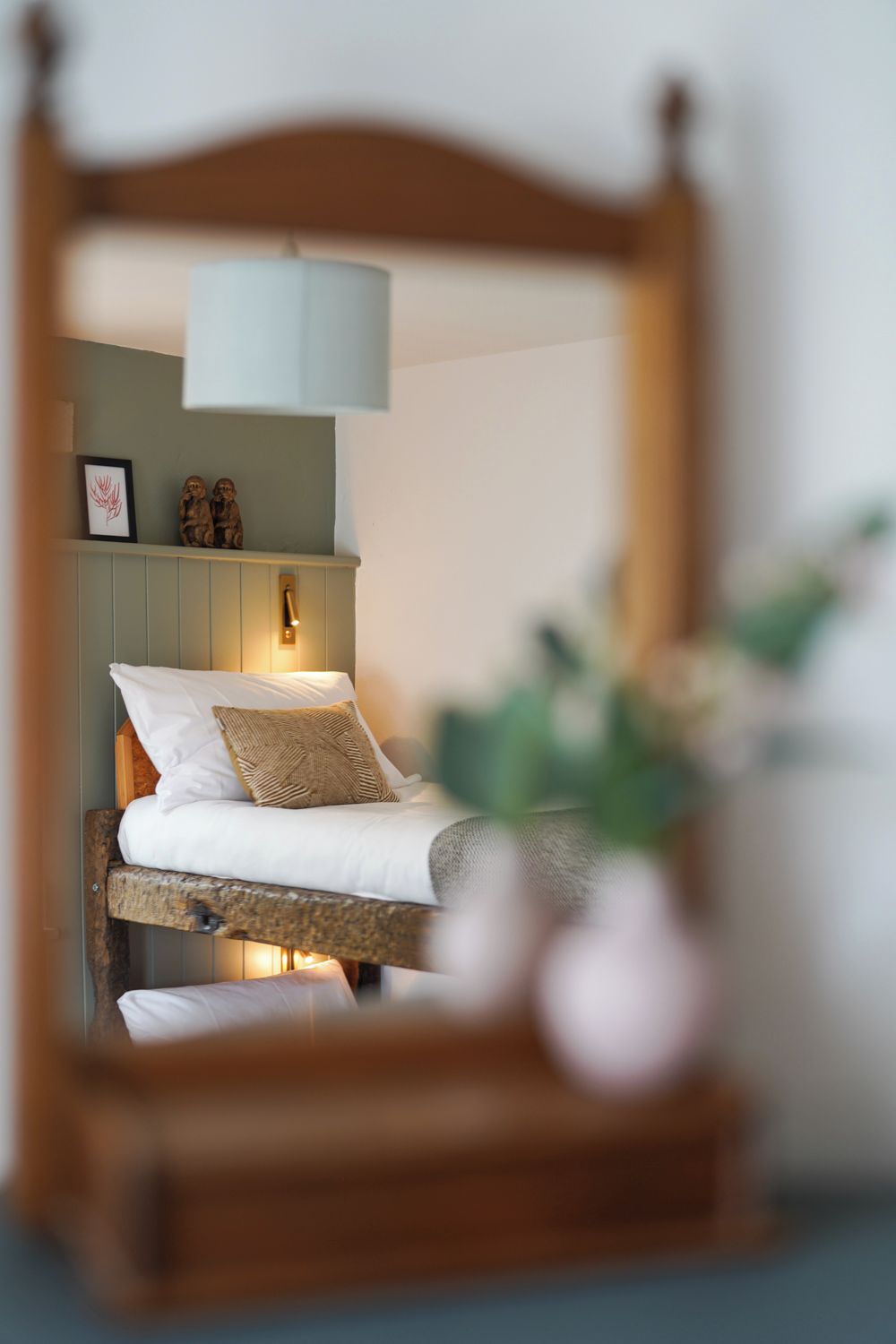 Uma cama com cabeceira de madeira, uma luminária de cabeceira e uma pequena prateleira com objetos decorativos.