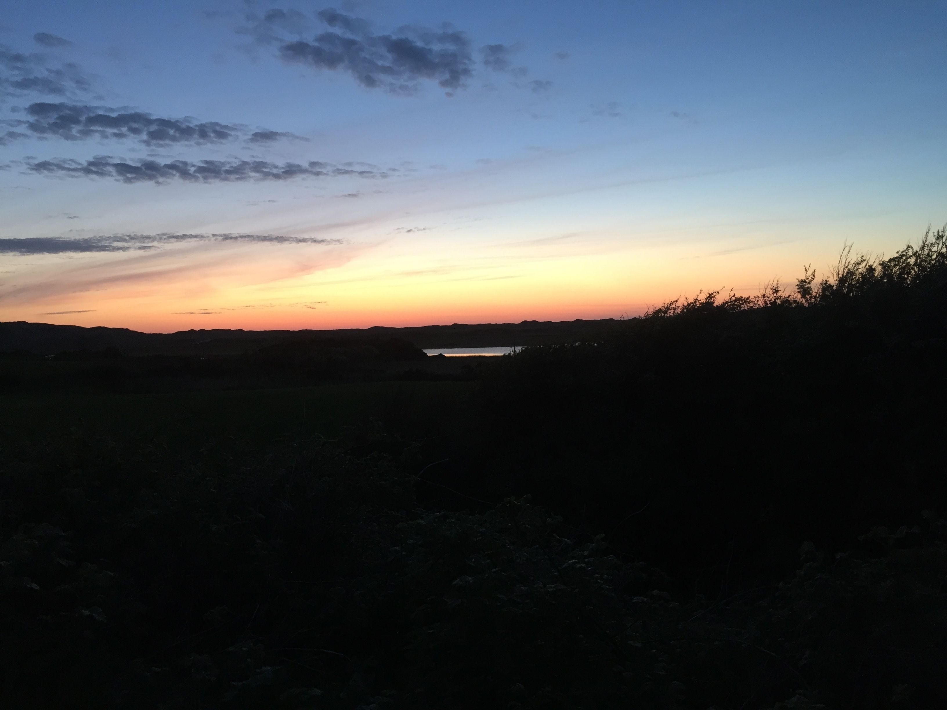 A sunset over a flat landscape with a body of water in the distance.