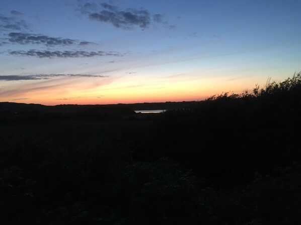 Un atardecer sobre un paisaje llano con una masa de agua al fondo.