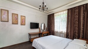 Ein Schlafzimmer mit Bett, Schreibtisch, Fernseher und einem Fenster mit Vorhängen.