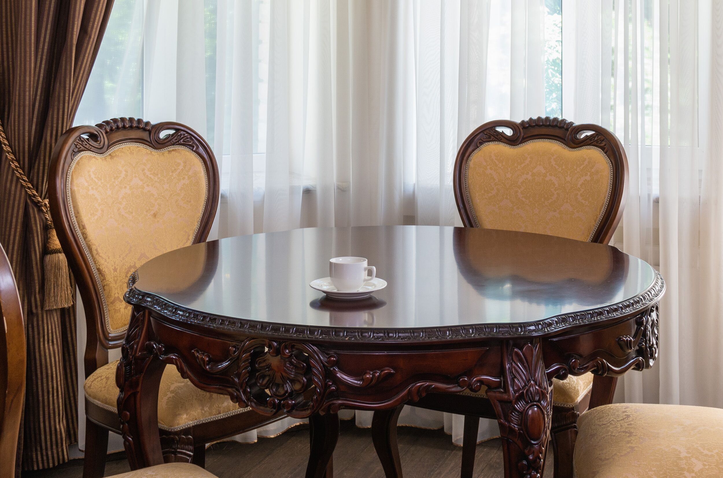 A round wooden table with a white cup on it, surrounded by two upholstered chairs with a heart-shaped backrest.