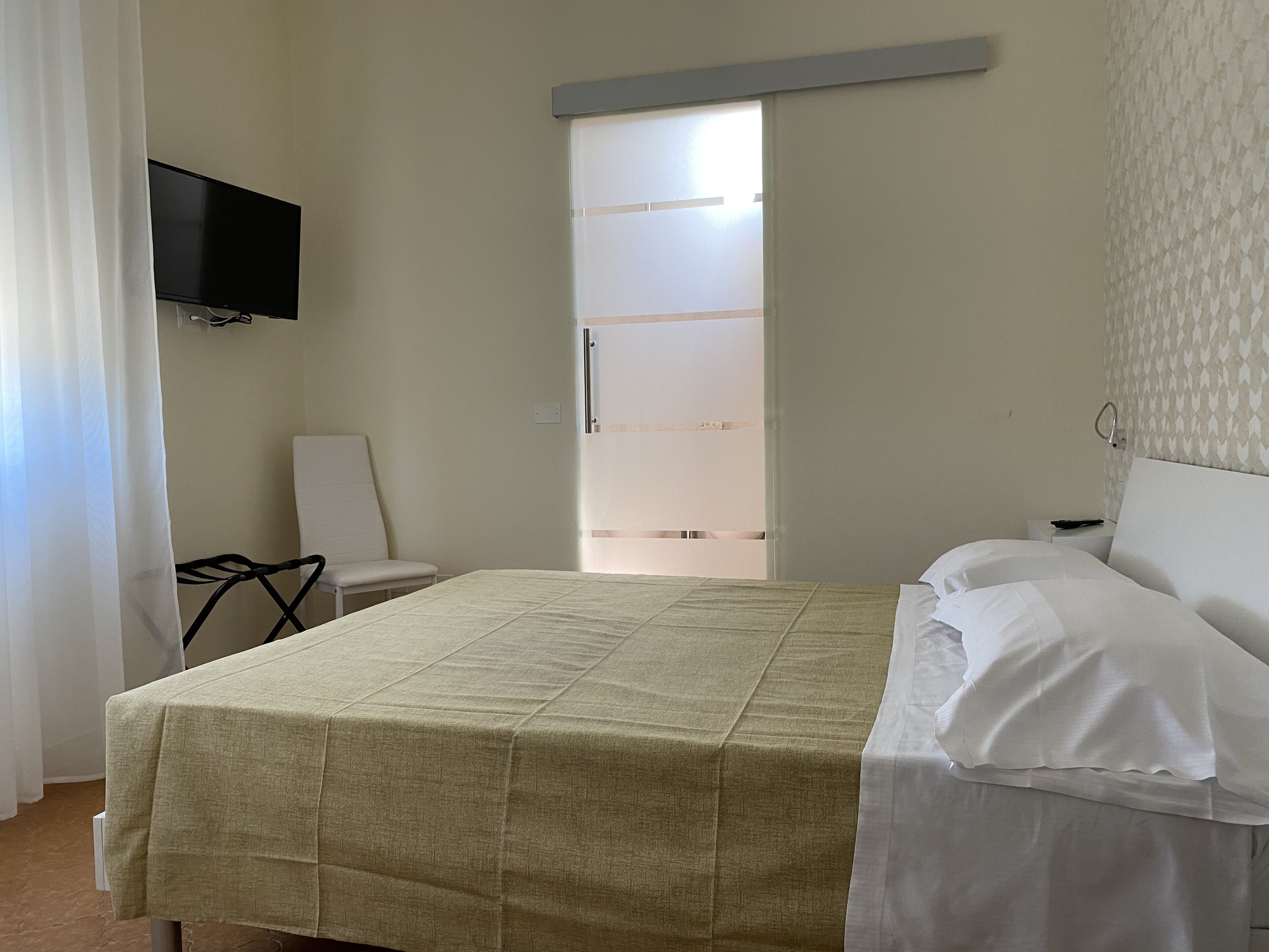 A hotel room with a bed, a chair, a television mounted on the wall, and a door with frosted glass panels.