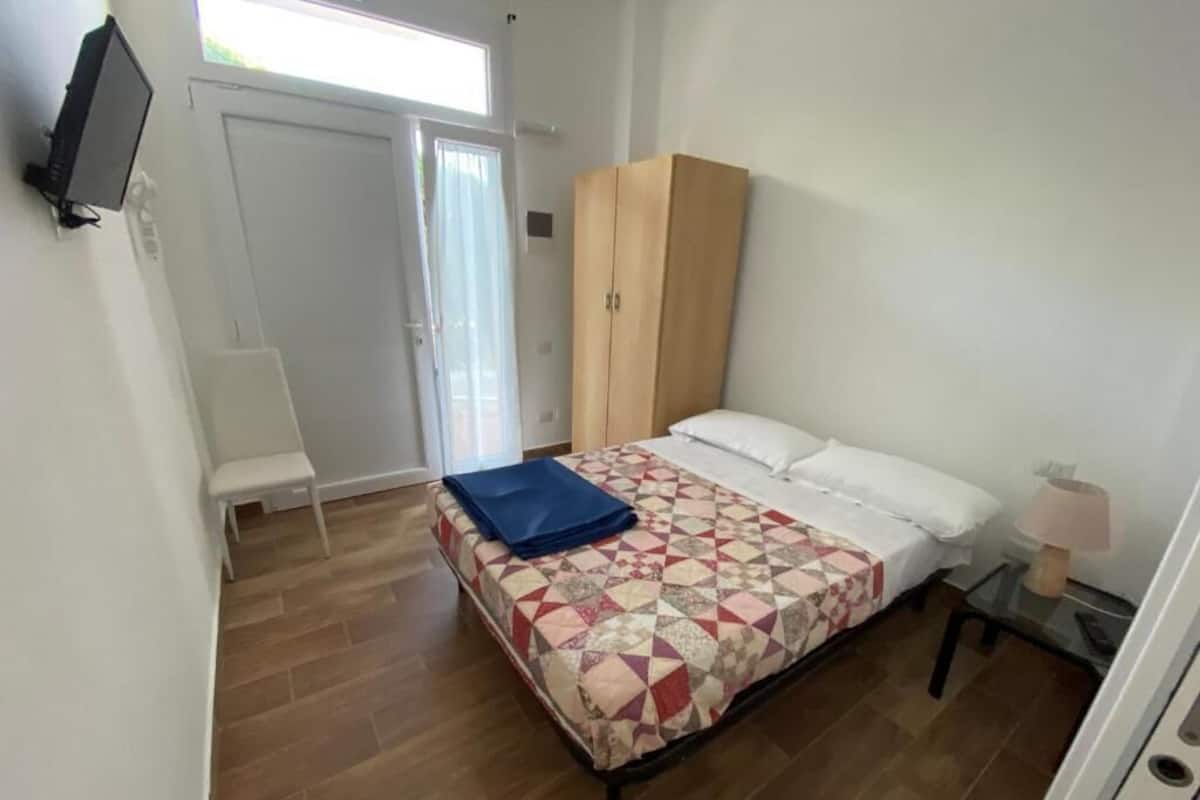 Ein Schlafzimmer mit einem Bett, einem Holzschrank, einem kleinen Tisch mit Lampe und einer Bank.