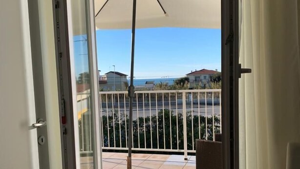 Un balcon avec un parasol blanc, une rambarde en métal et une vue sur la mer et les bâtiments.