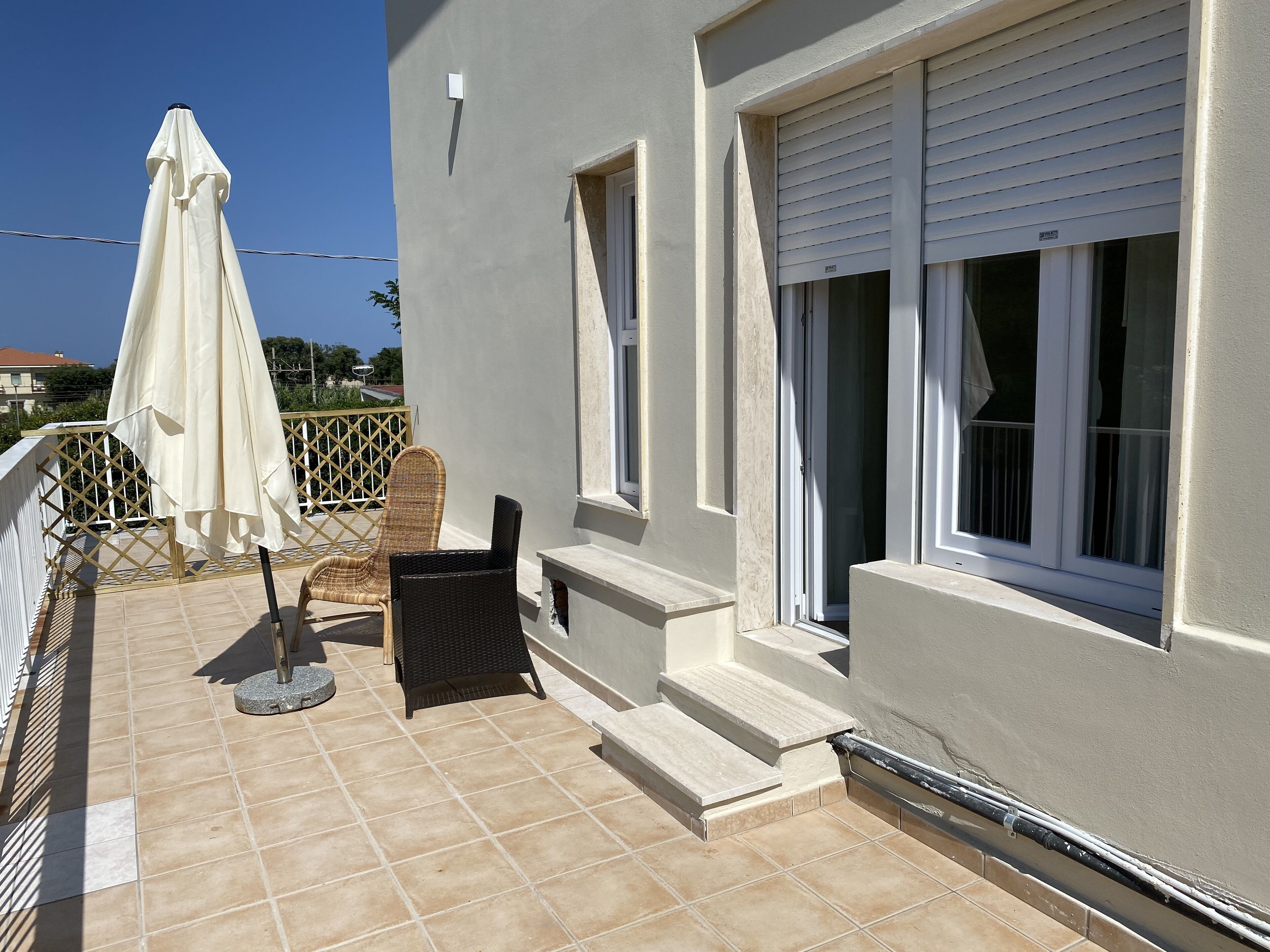 A balcony with a wicker chair, a small table, and a white umbrella.