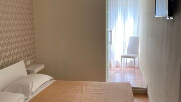Habitación de hotel con cama, televisor montado en la pared y vistas al exterior a través de una ventana con cortinas.