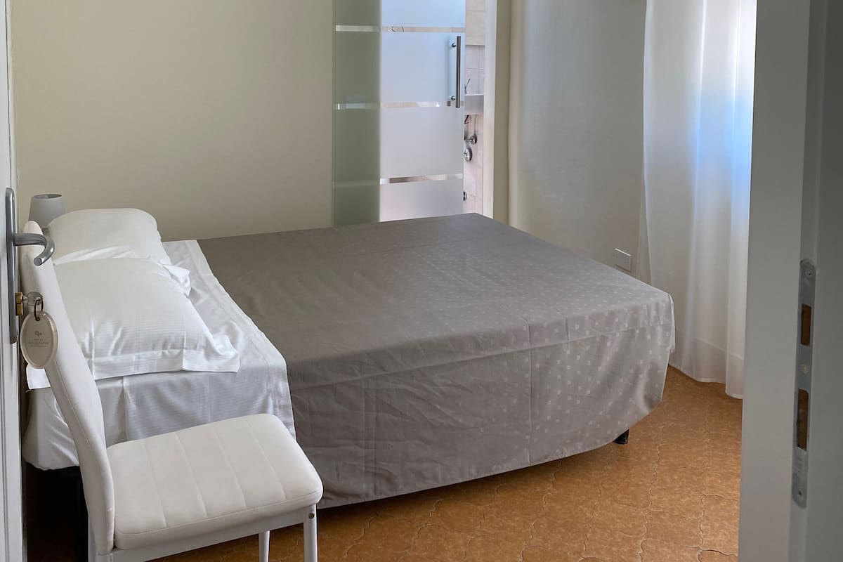 Ein Schlafzimmer mit Bett, Sitzbank, Fernseher und einem durch eine Glastür einsehbaren Badezimmer.